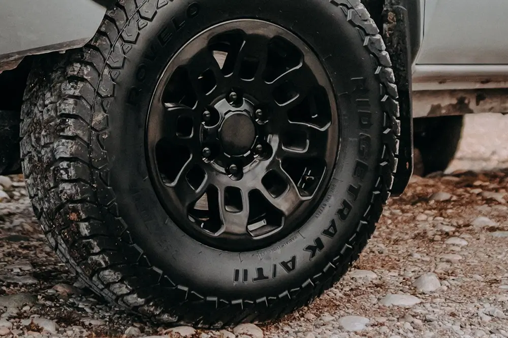Black truck tires TigerTrak A/T II with aggressive all-terrain tread on muddy rocky ground