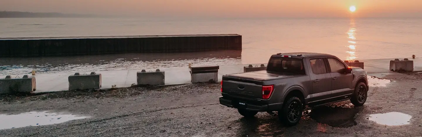 A truck parked on a pier with sun setting over water