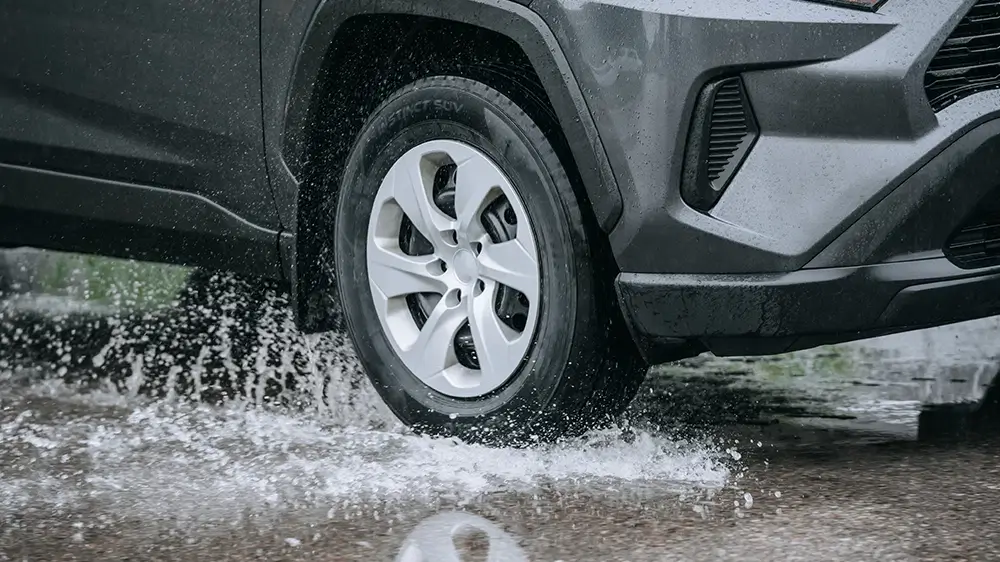 SUV equipped with performance tires splashing through water on a rainy road, demonstrating traction and control