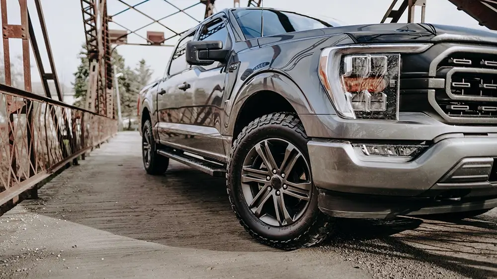 Truck with all terrain tires parked on a bridge, showcasing rugged design and strong grip for off-road adventures.