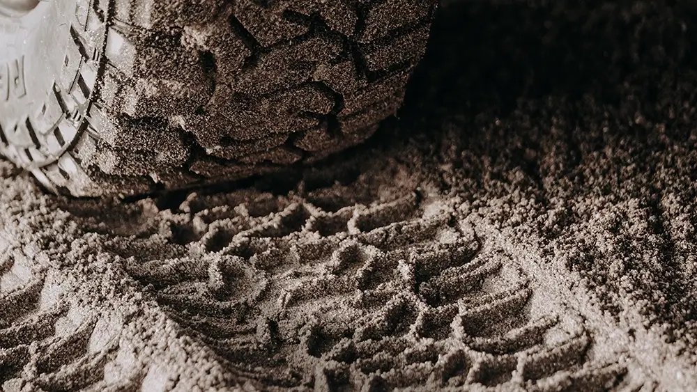 Tire leaving deep tread marks in sandy terrain, showcasing durability of all terrain tires used for off-road driving.