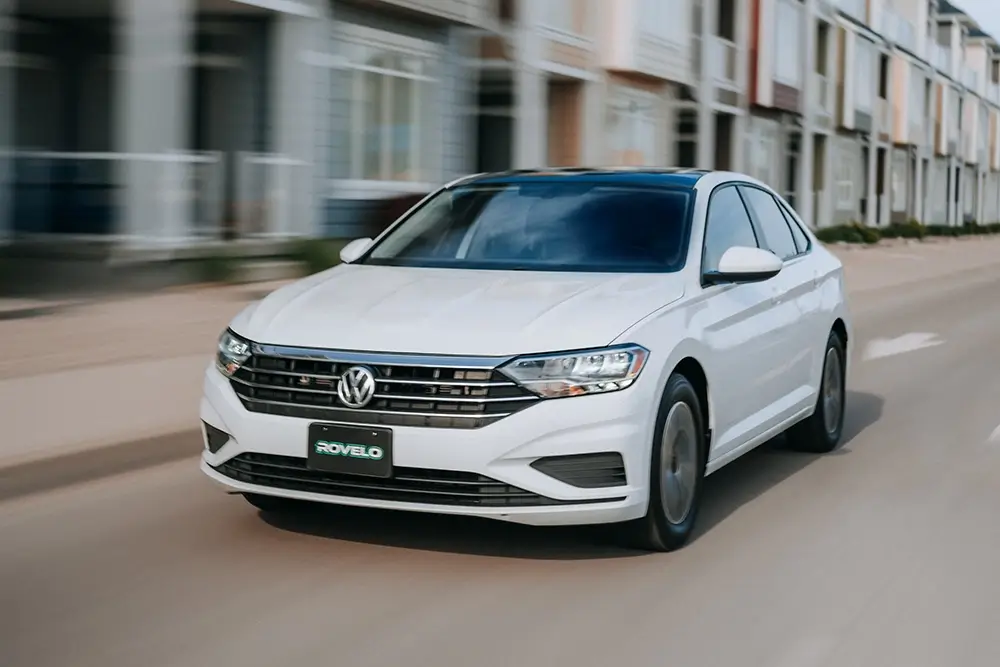 Volkswagen sedan driving on a city street, showcasing all season tires suitable for various road conditions.